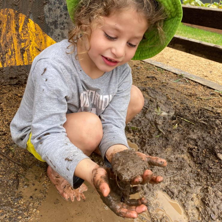 A young girl at Grace Village Early Learning gets involved with some mud and play based learning